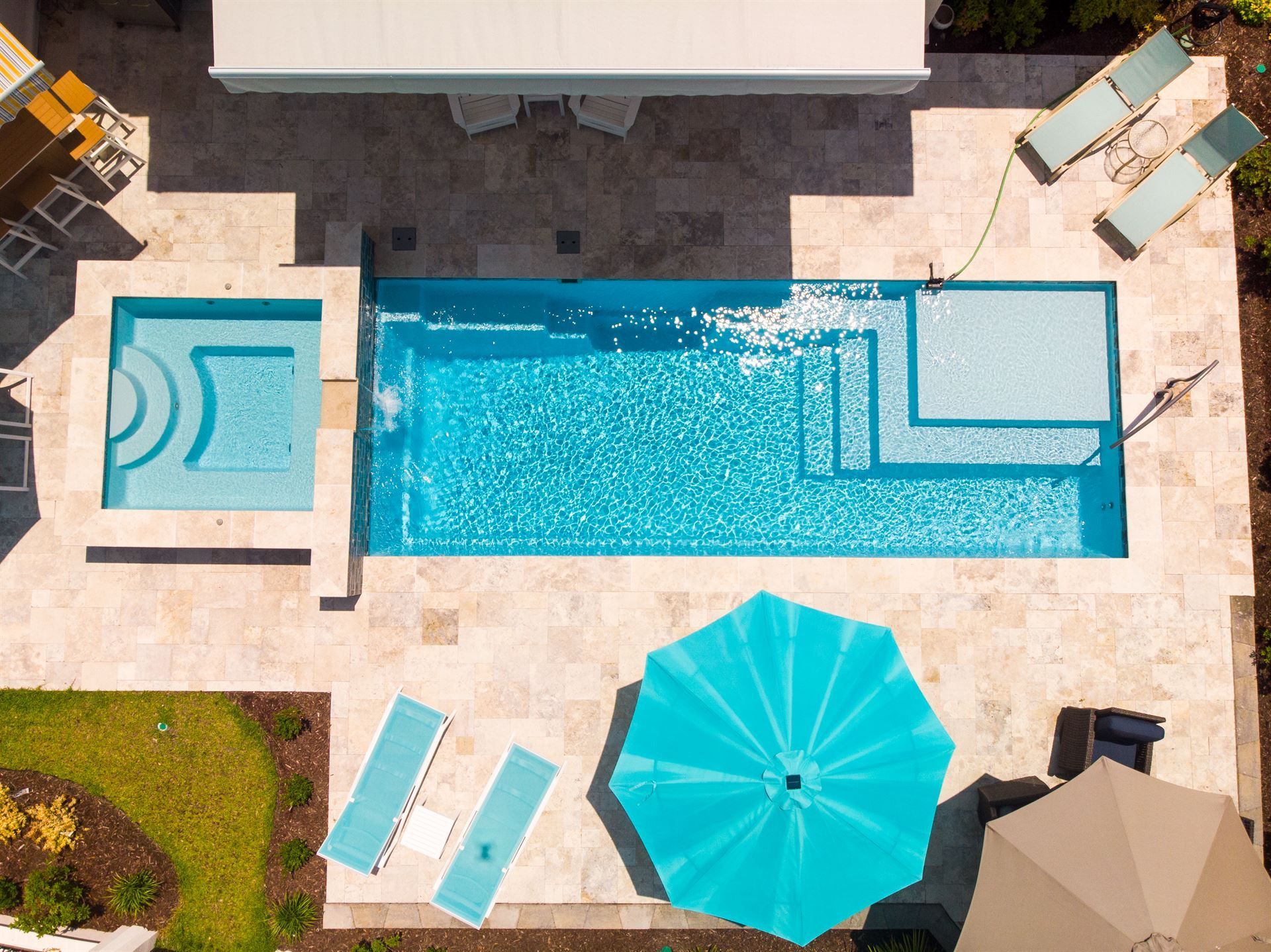 Aerial view of a backyard pool with turquoise water, lounge chairs, and umbrellas on a sunny patio.