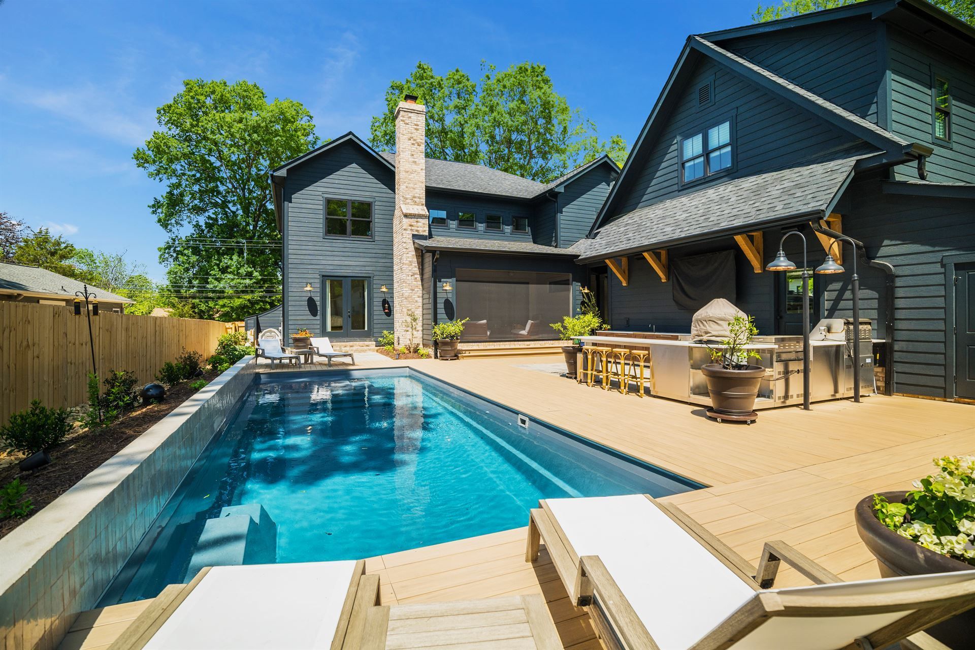 Modern backyard with a rectangular swimming pool, patio lounge chairs, and a dark gray house under a clear sky