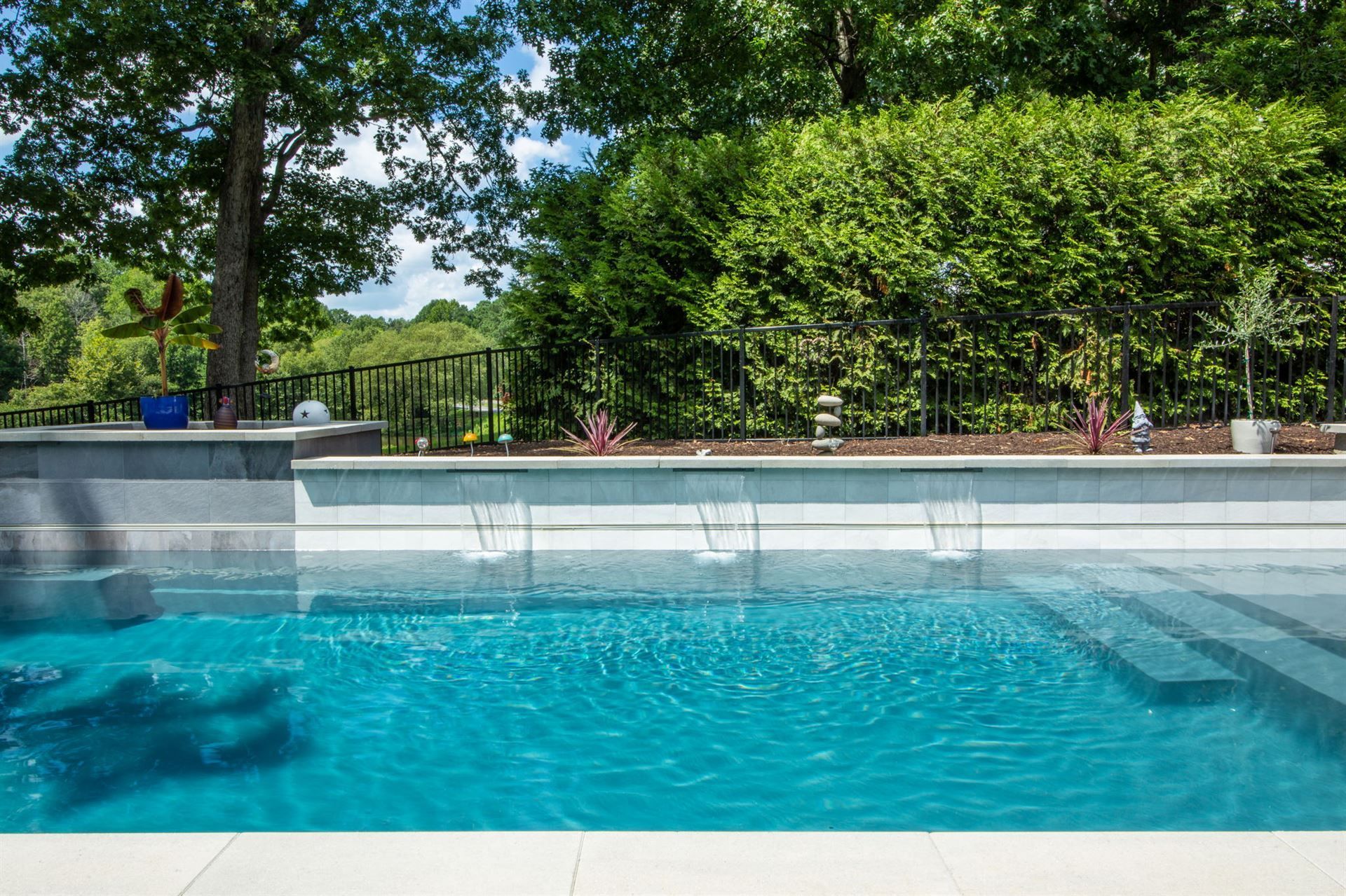 Backyard swimming pool with blue water and lush green hedge under a sunny sky