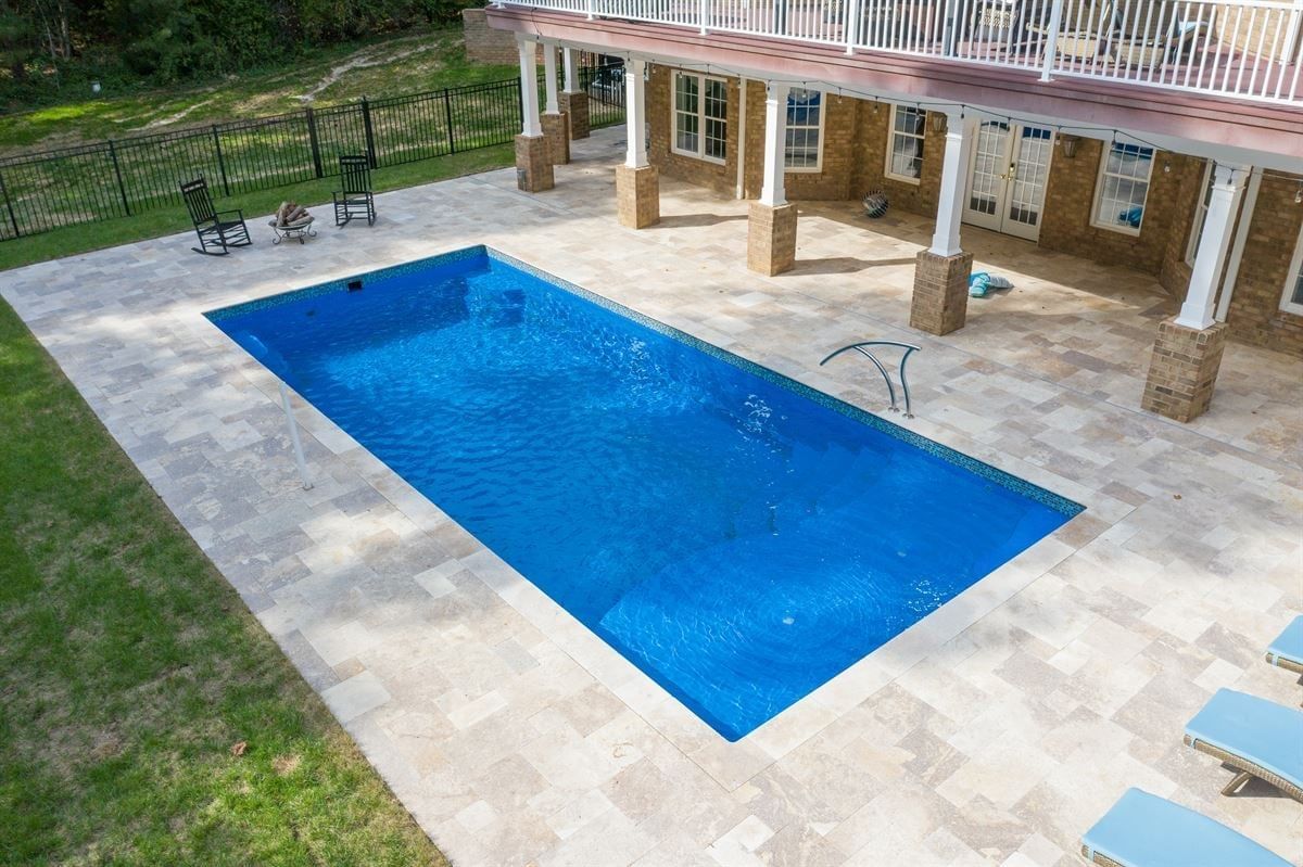 Backyard swimming pool with blue water, stone patio, and shaded seating area