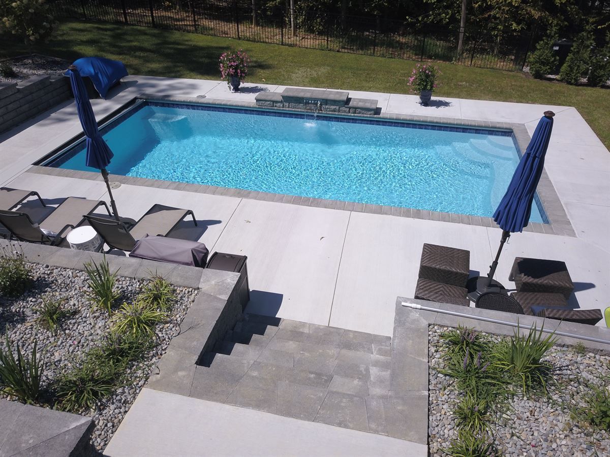 Backyard pool with blue water, lounge chairs, and a patio with umbrellas and steps