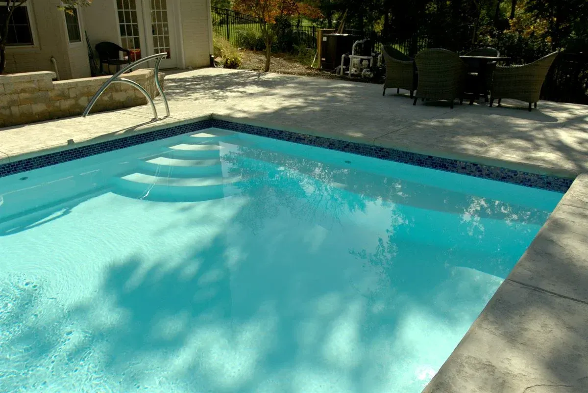 Backyard swimming pool with clear blue water and patio chairs in the background