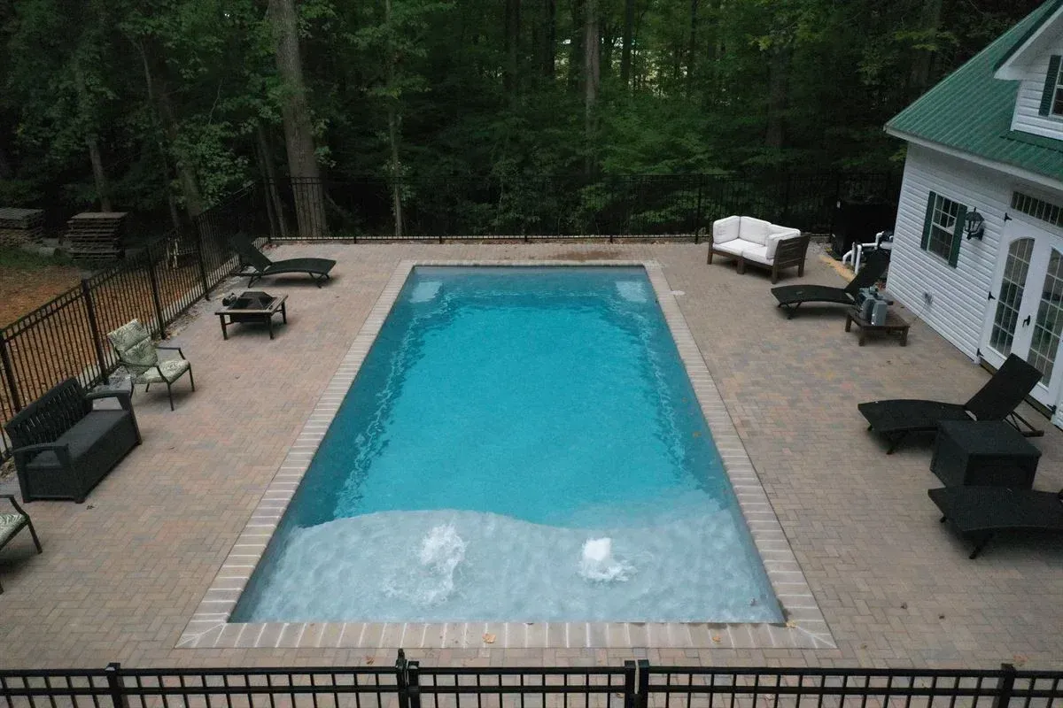 Backyard swimming pool with tan deck, lounge chairs, and surrounding trees