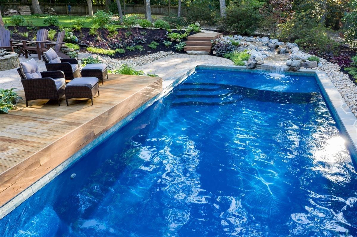 Backyard swimming pool with lounge chairs and a stone patio, surrounded by lush greenery
