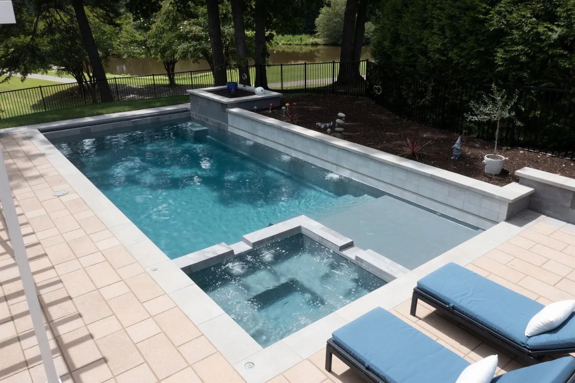 Backyard pool with a raised hot tub, blue water, and lounge chairs on a sunny patio.