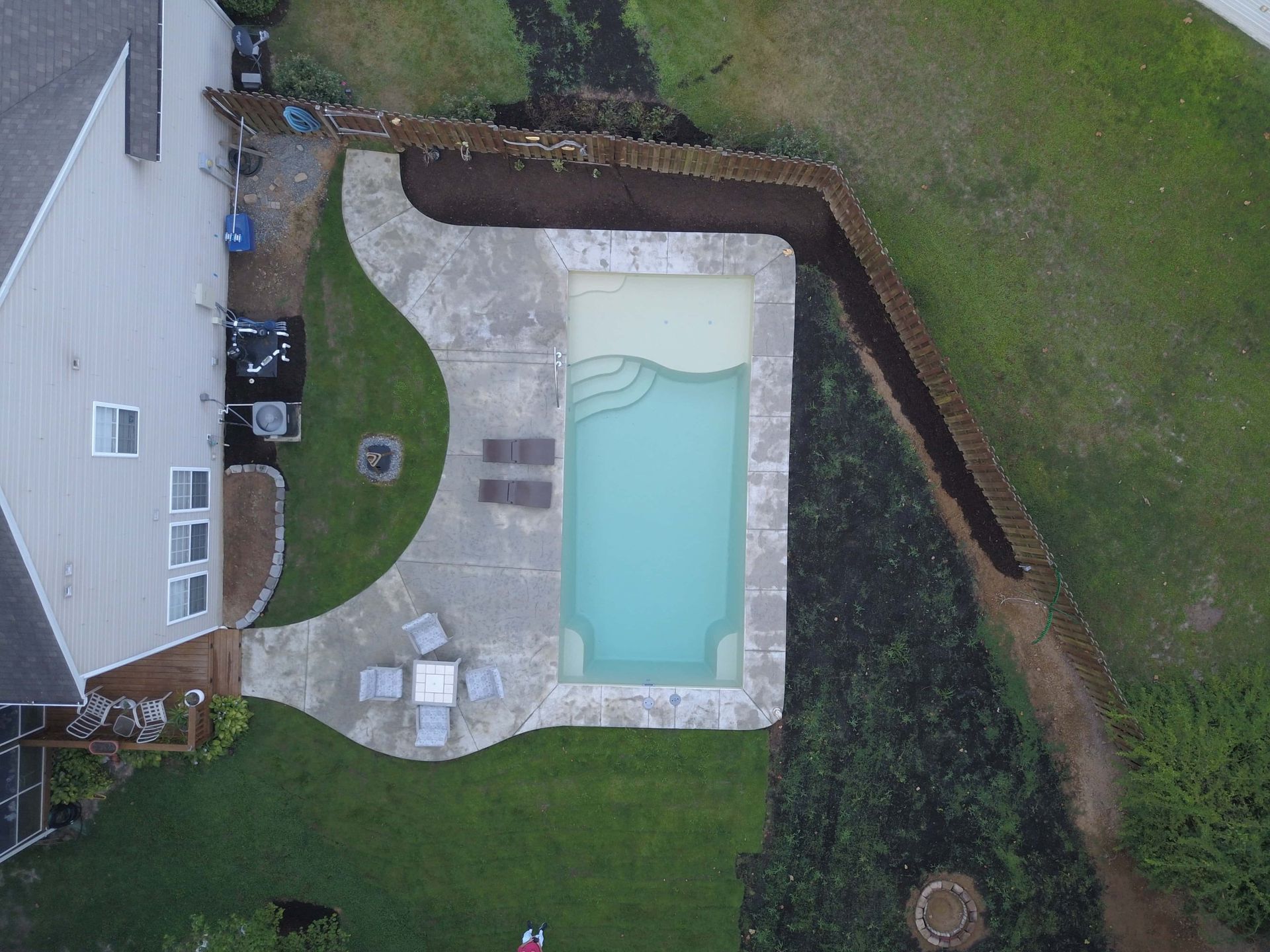 Aerial view of a backyard with a rectangular pool, patio, lawn, and fence beside a house.