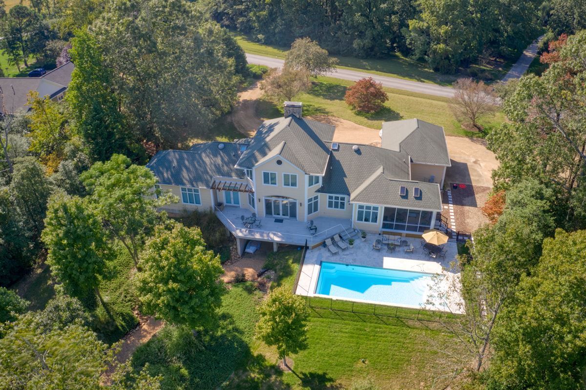 Aerial view of a large white house with a backyard pool, surrounded by trees and lawn.