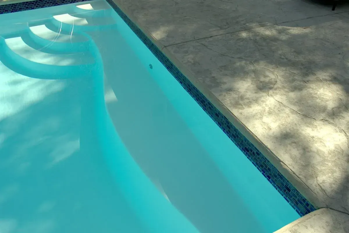 Blue swimming pool with curved steps beside a concrete deck in sunlight