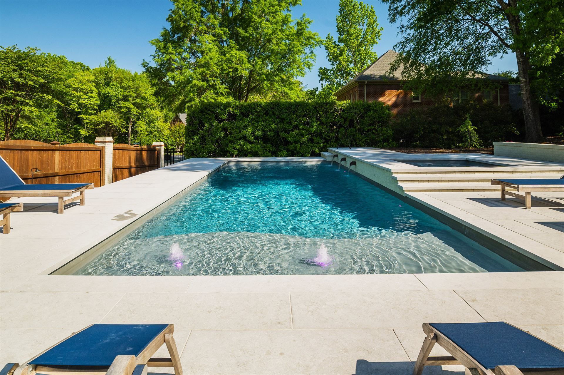 Backyard swimming pool with spa jets, white deck, and lounge chairs surrounded by trees