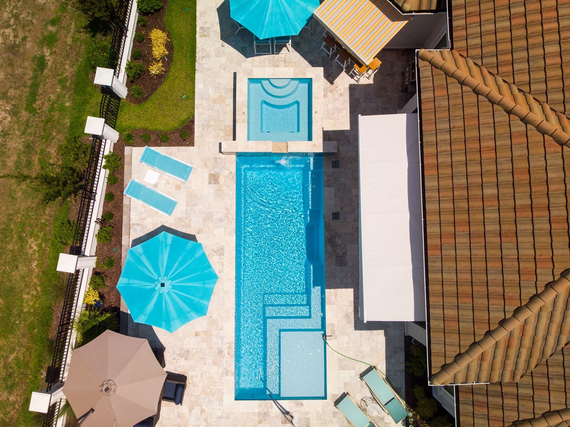 Aerial view of a rectangular hotel pool with turquoise umbrellas, lounge chairs, and a tiled patio.