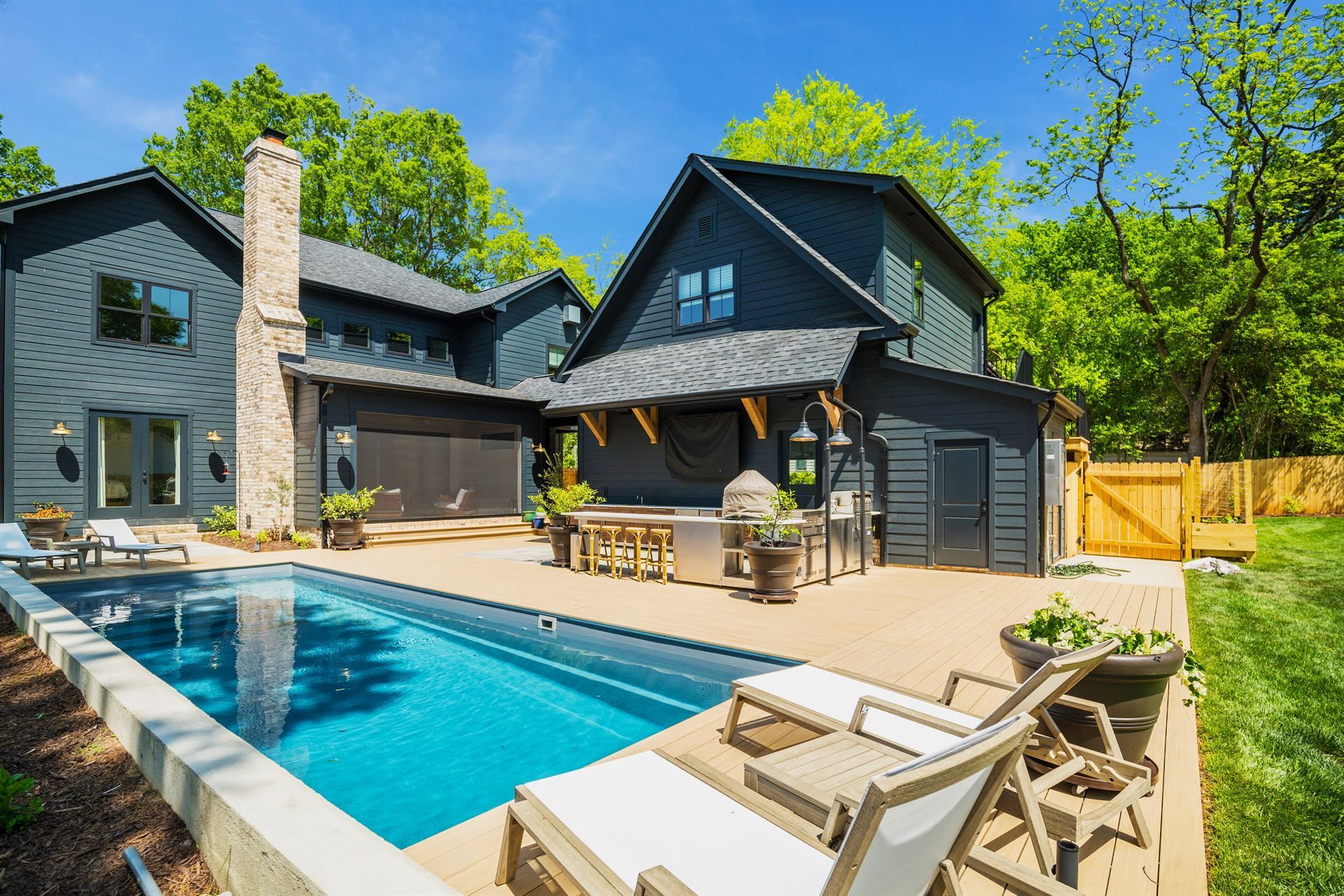 Modern dark-gray house with backyard pool, patio seating, and bright green trees