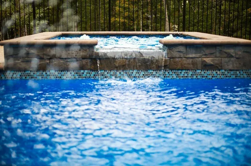 Blue swimming pool with bubbling spa jets and a stone waterfall edge at the far side