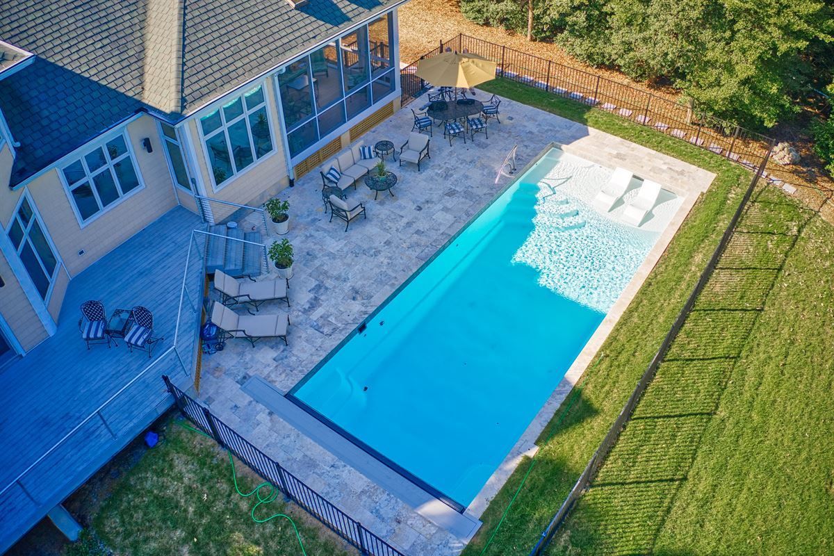 Aerial view of a backyard with a long blue swimming pool beside a patio and house.