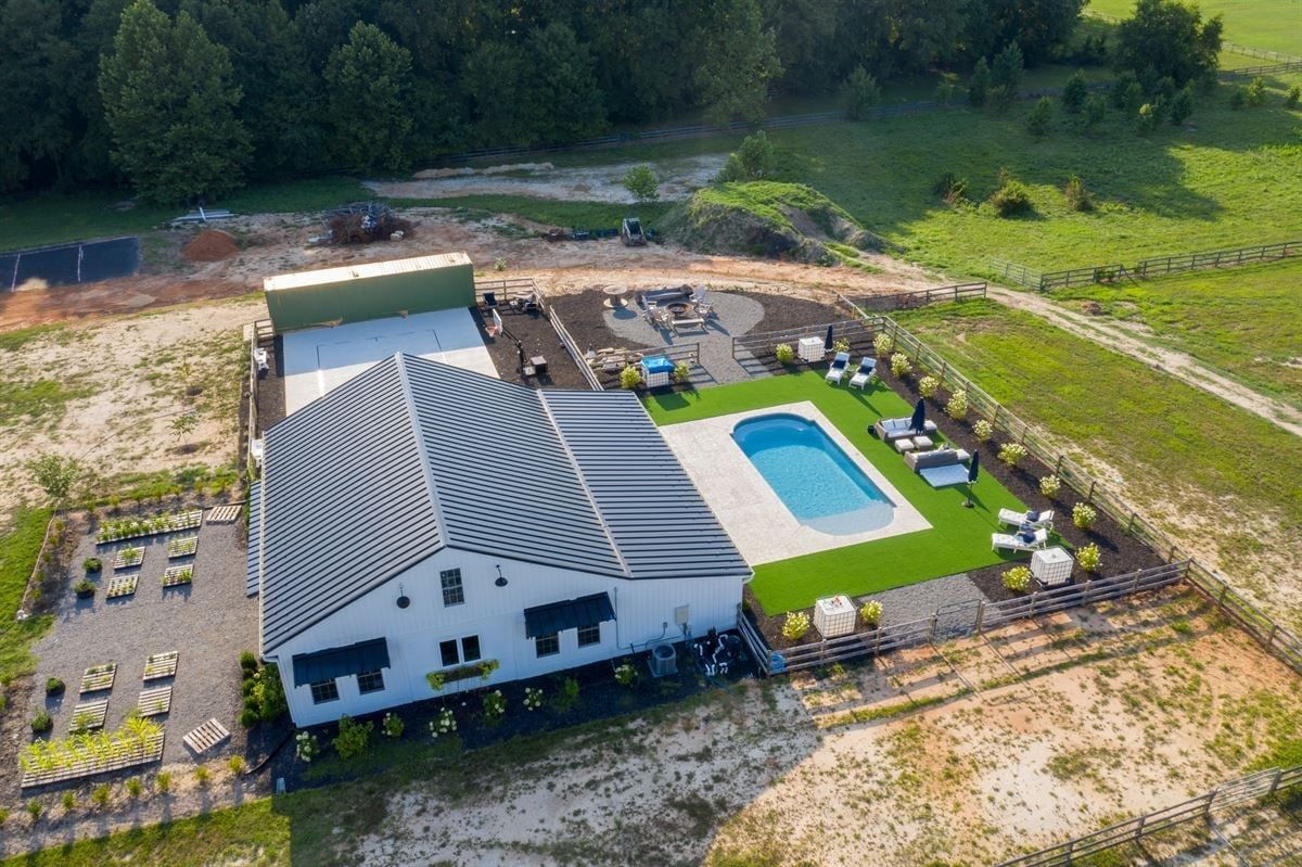 Aerial view of a white house with a gray roof and backyard pool beside a wooded area