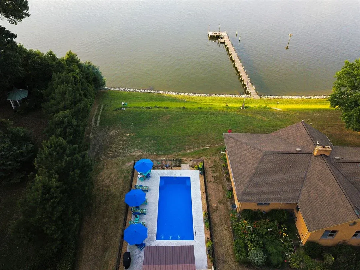 Aerial view of a lakeside house with a pool, dock, and green lawn beside calm water
