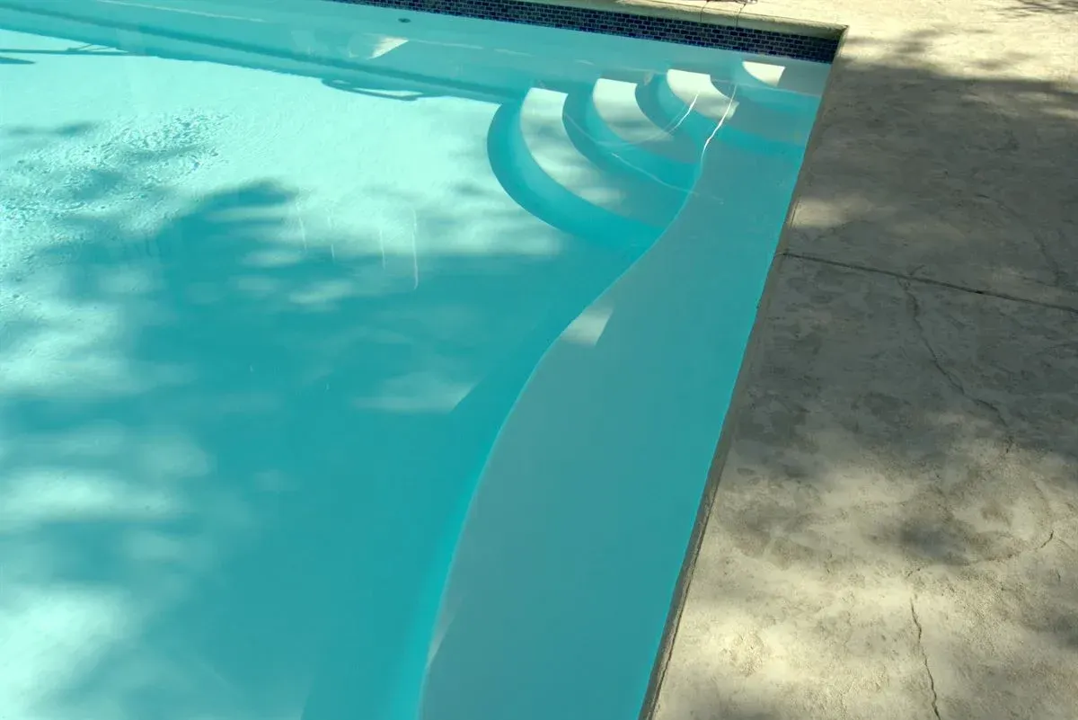 Swimming pool corner with clear blue water, pool steps, and sunlit concrete deck