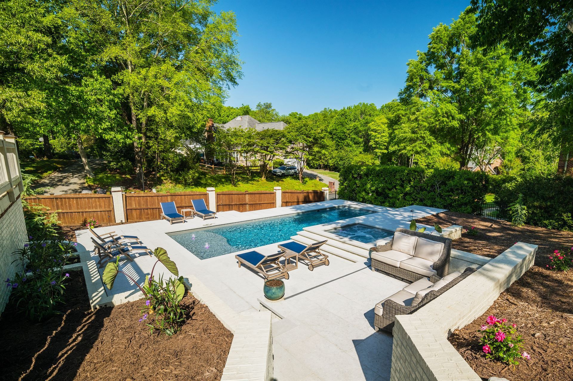 Backyard patio with blue pool, lounge chairs, and stone seating under bright green trees