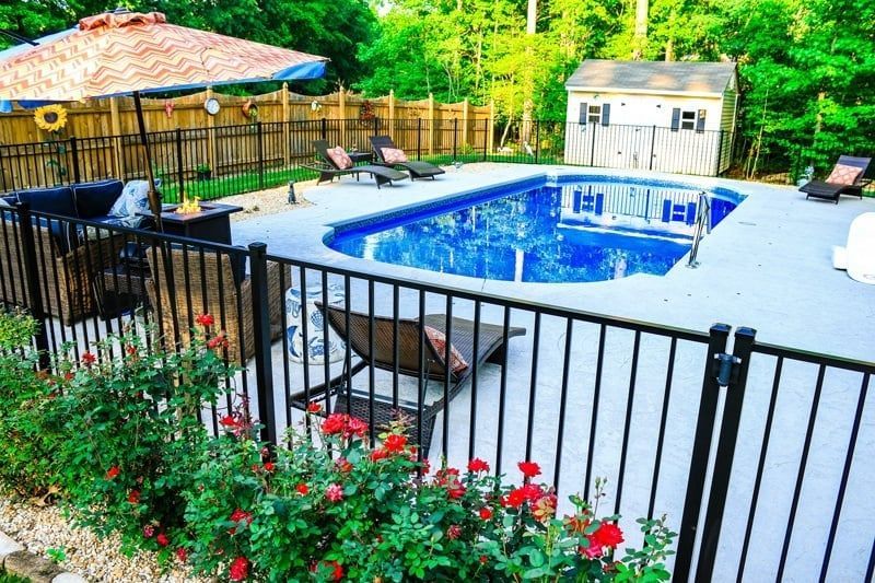 Backyard with fenced-in blue swimming pool, lounge chairs, patio umbrella, and red flowers in the foreground