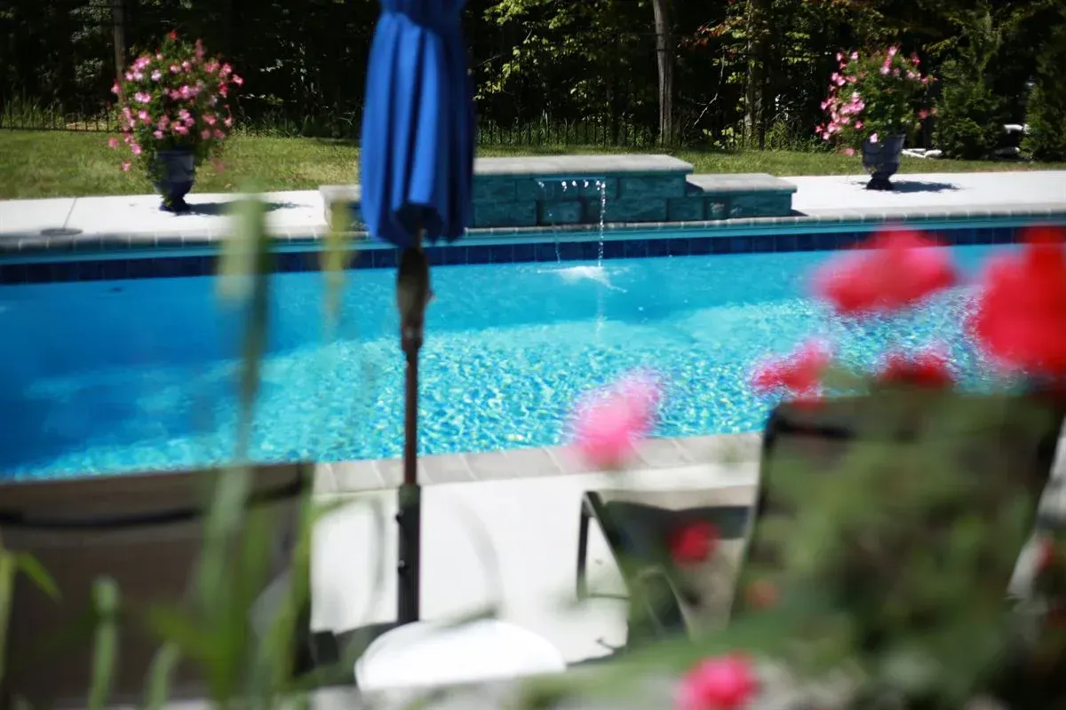 Backyard pool with blue water, patio chairs, and blurred flowers in the foreground