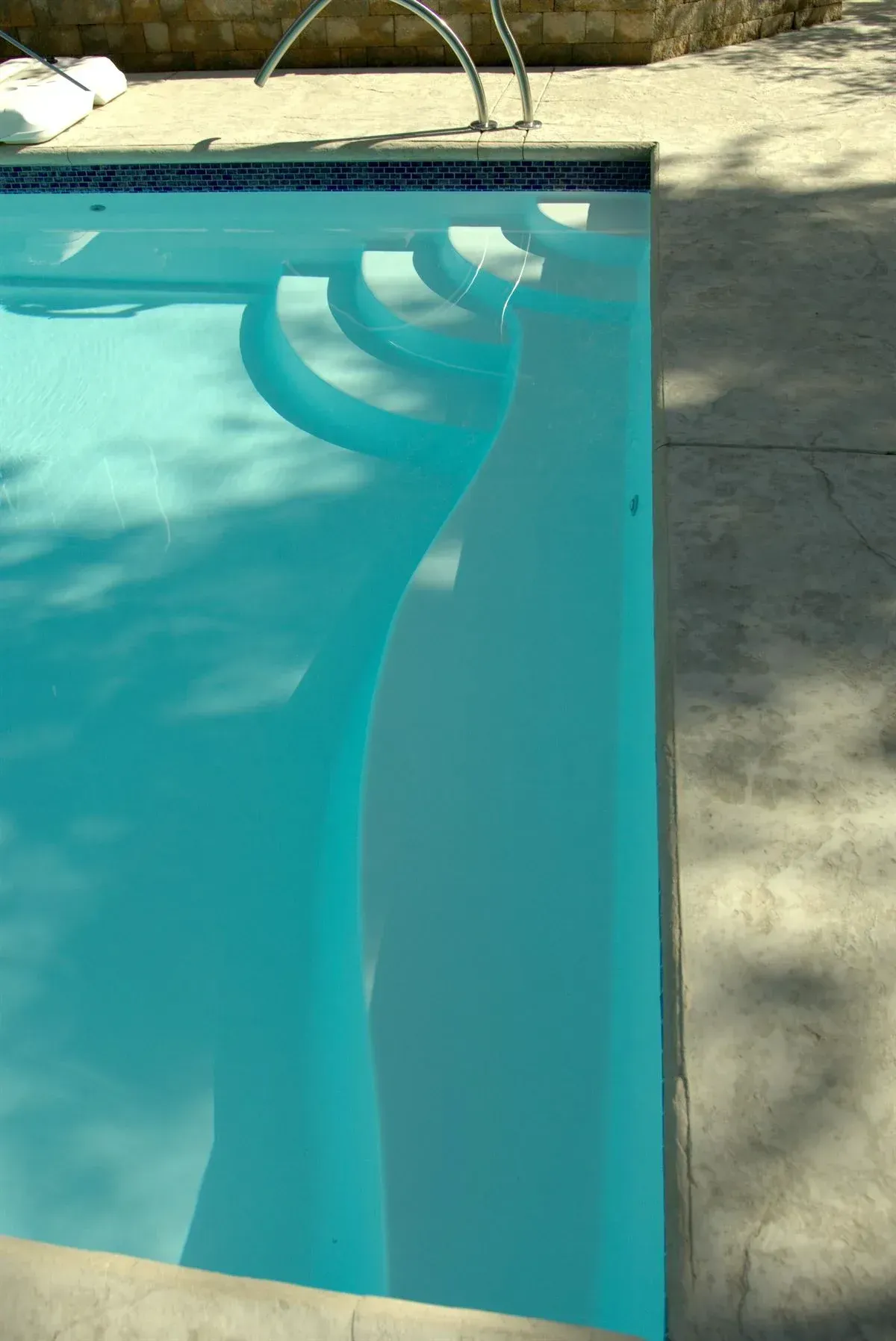 Swimming pool corner with curved steps and turquoise water beside a stone deck