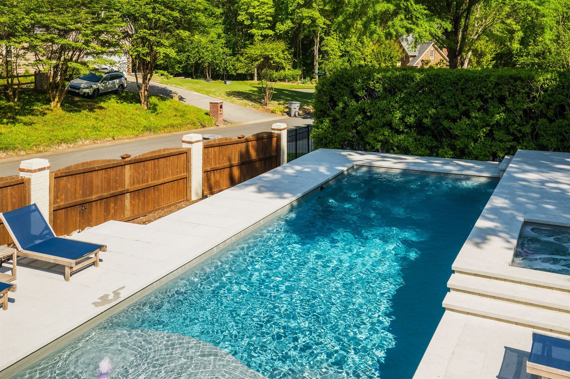 Backyard swimming pool with blue water, lounge chair, and green hedges in sunlight