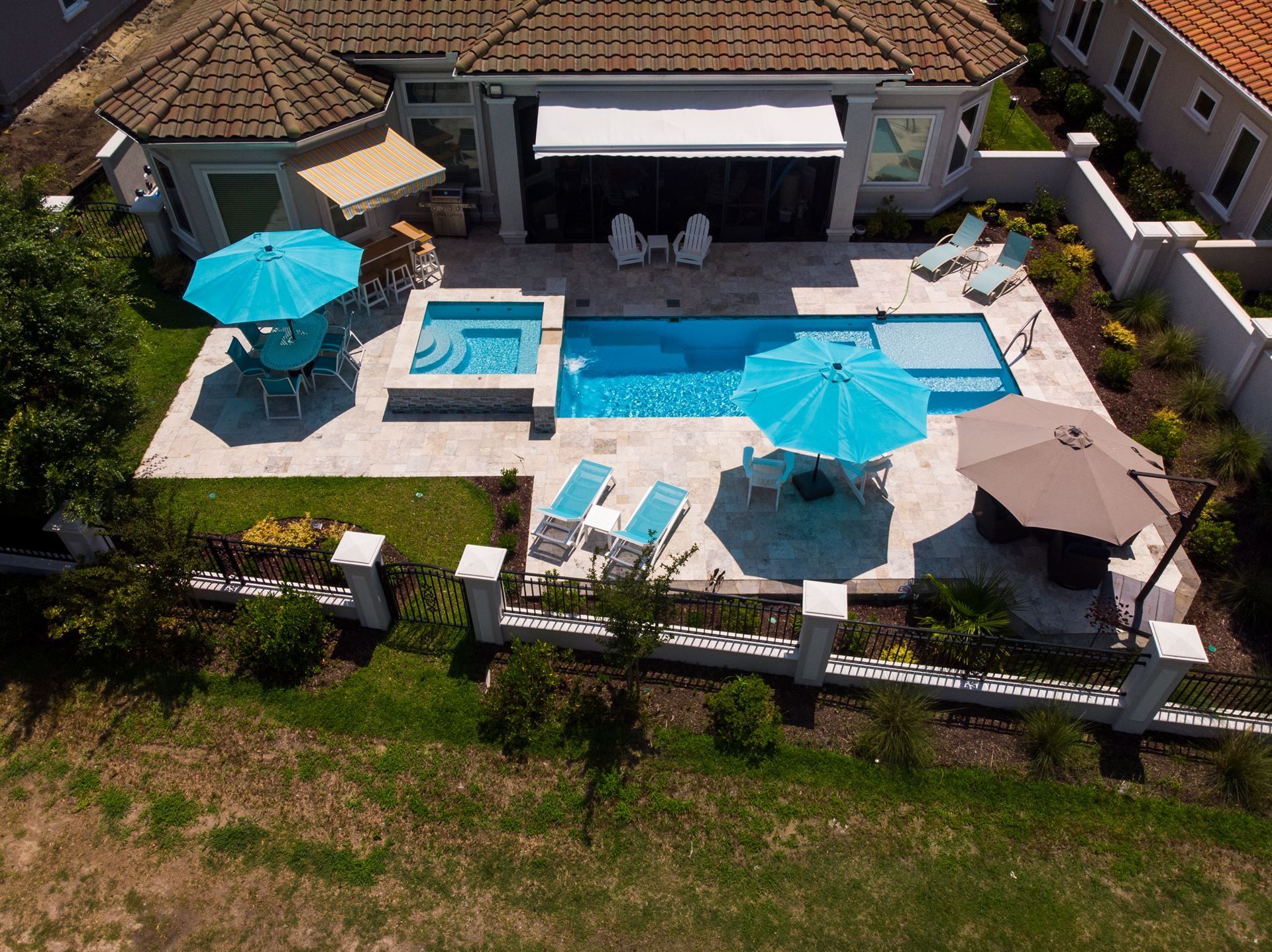 Aerial view of a backyard pool with turquoise umbrellas, lounge chairs, and a covered patio by a house