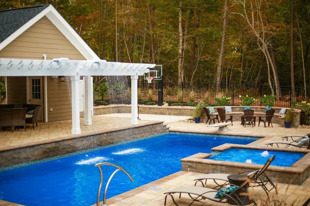 Backyard pool with blue water, lounge chairs, pergola, and a patio beside a tan house.