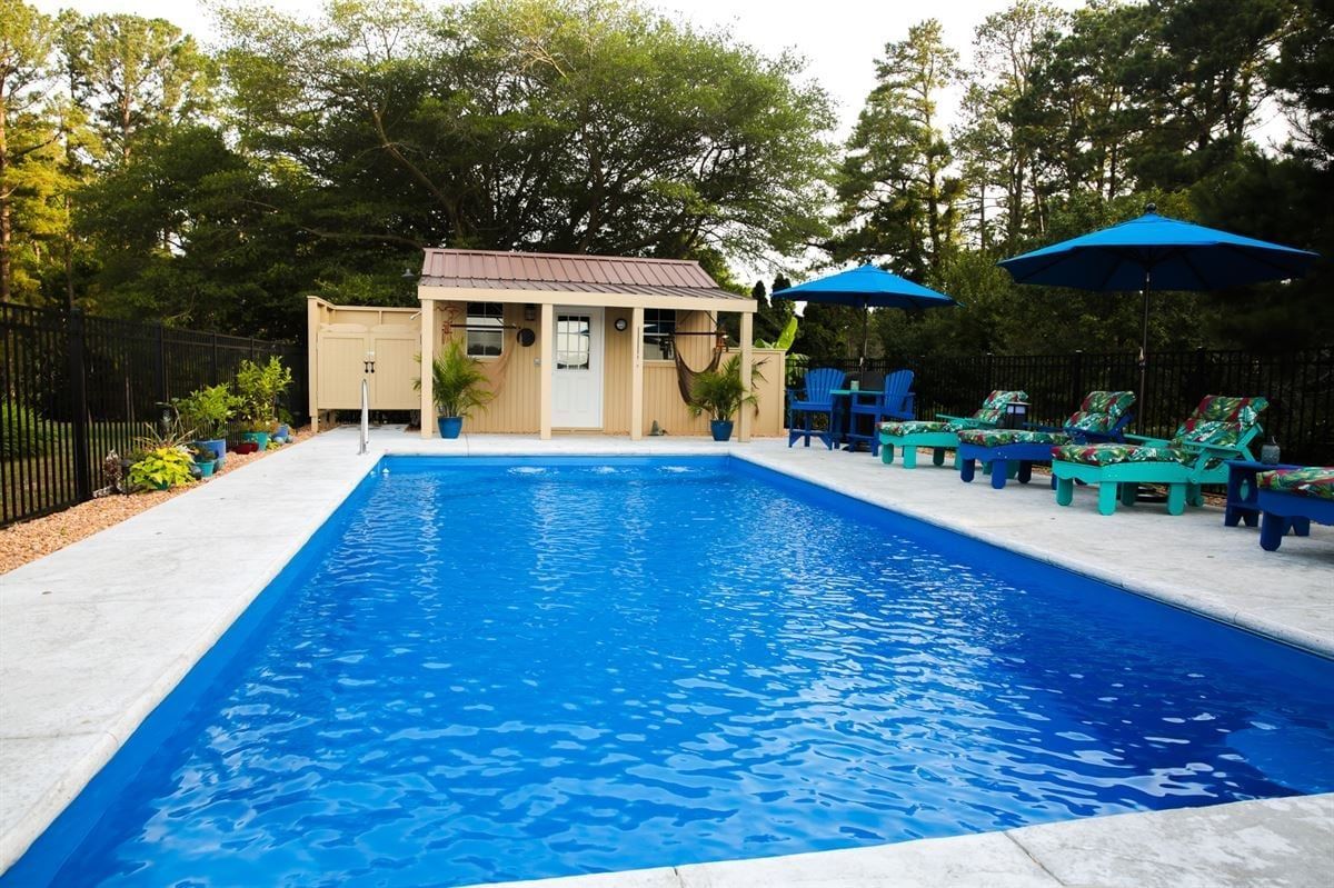 Outdoor swimming pool with blue water, lounge chairs, and umbrellas beside a small cabana.