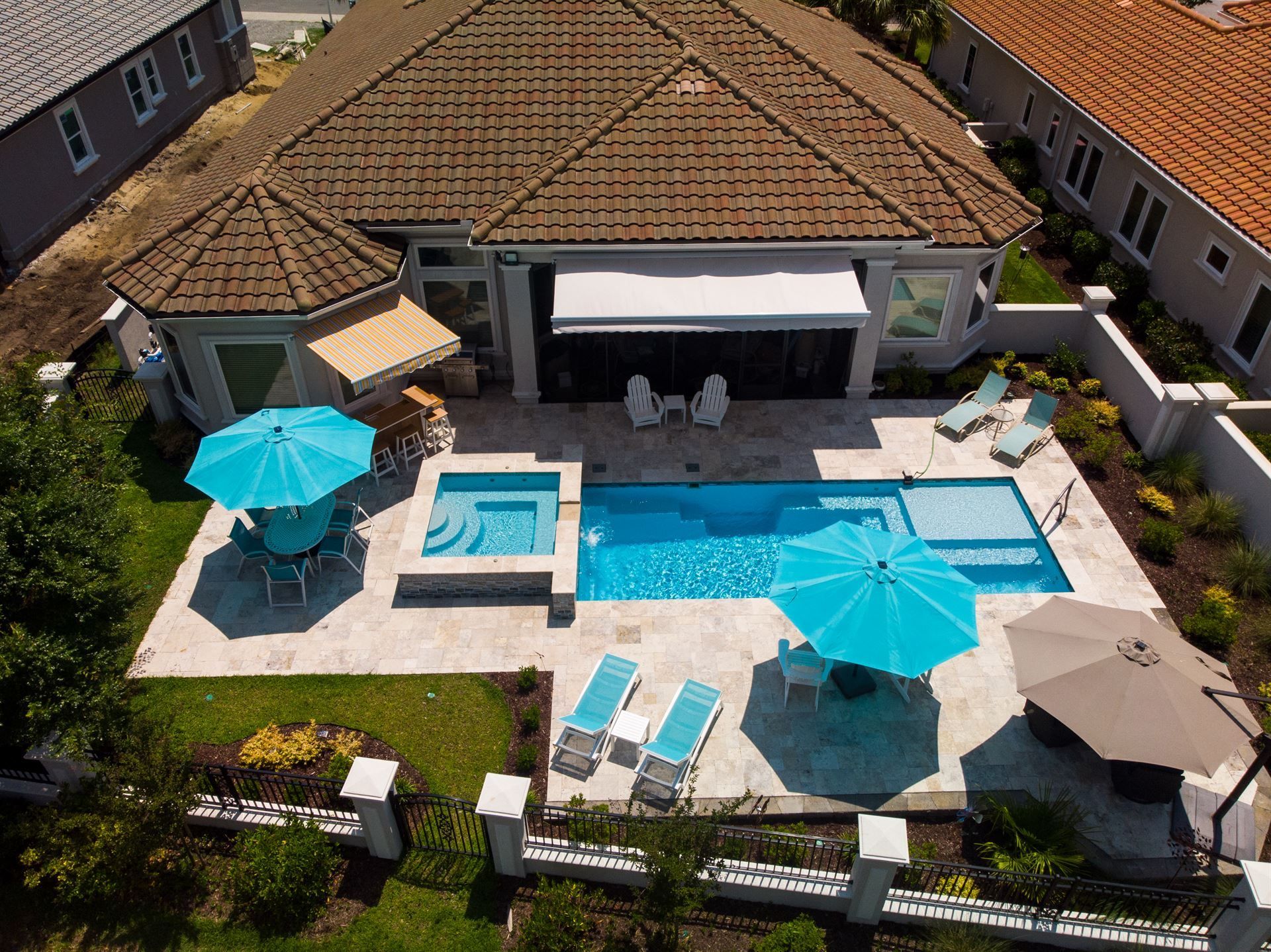 Aerial view of a backyard with a swimming pool, hot tub, umbrellas, and a patio beside a house.