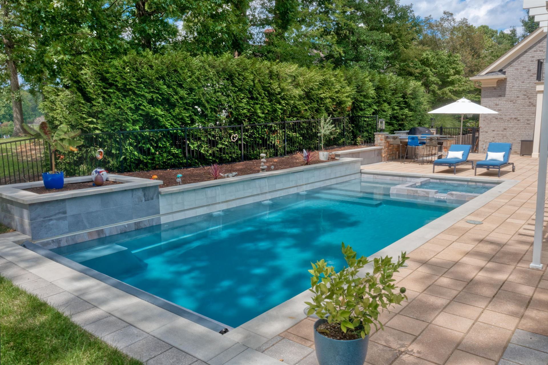 Backyard pool with blue water, lounge chairs, and patio surrounded by greenery