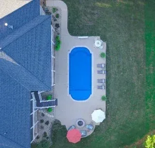 Aerial view of a backyard with a blue swimming pool, patio furniture, and a house roof.