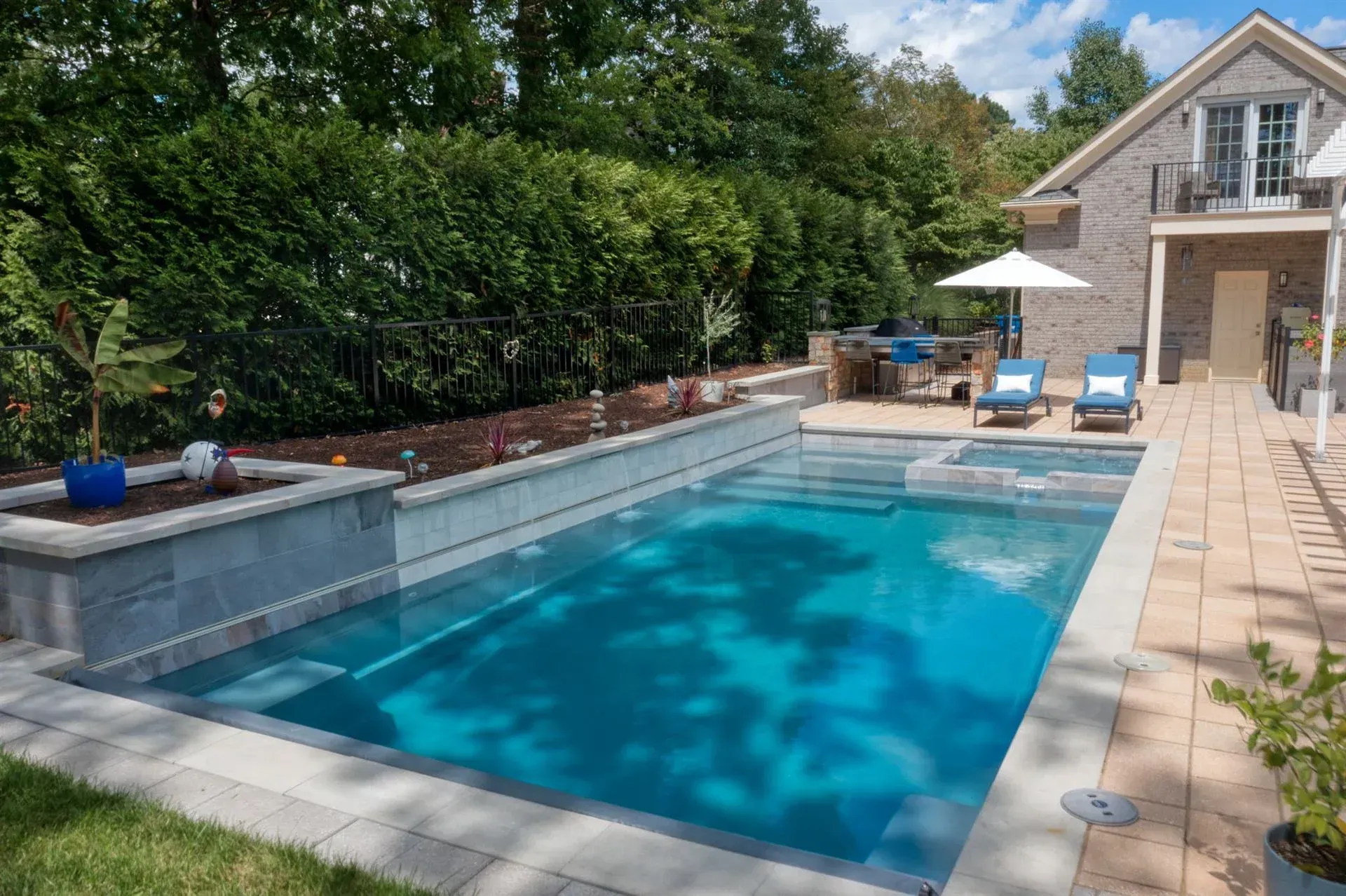 Backyard pool with blue water, patio chairs, and a house beside a brick privacy wall