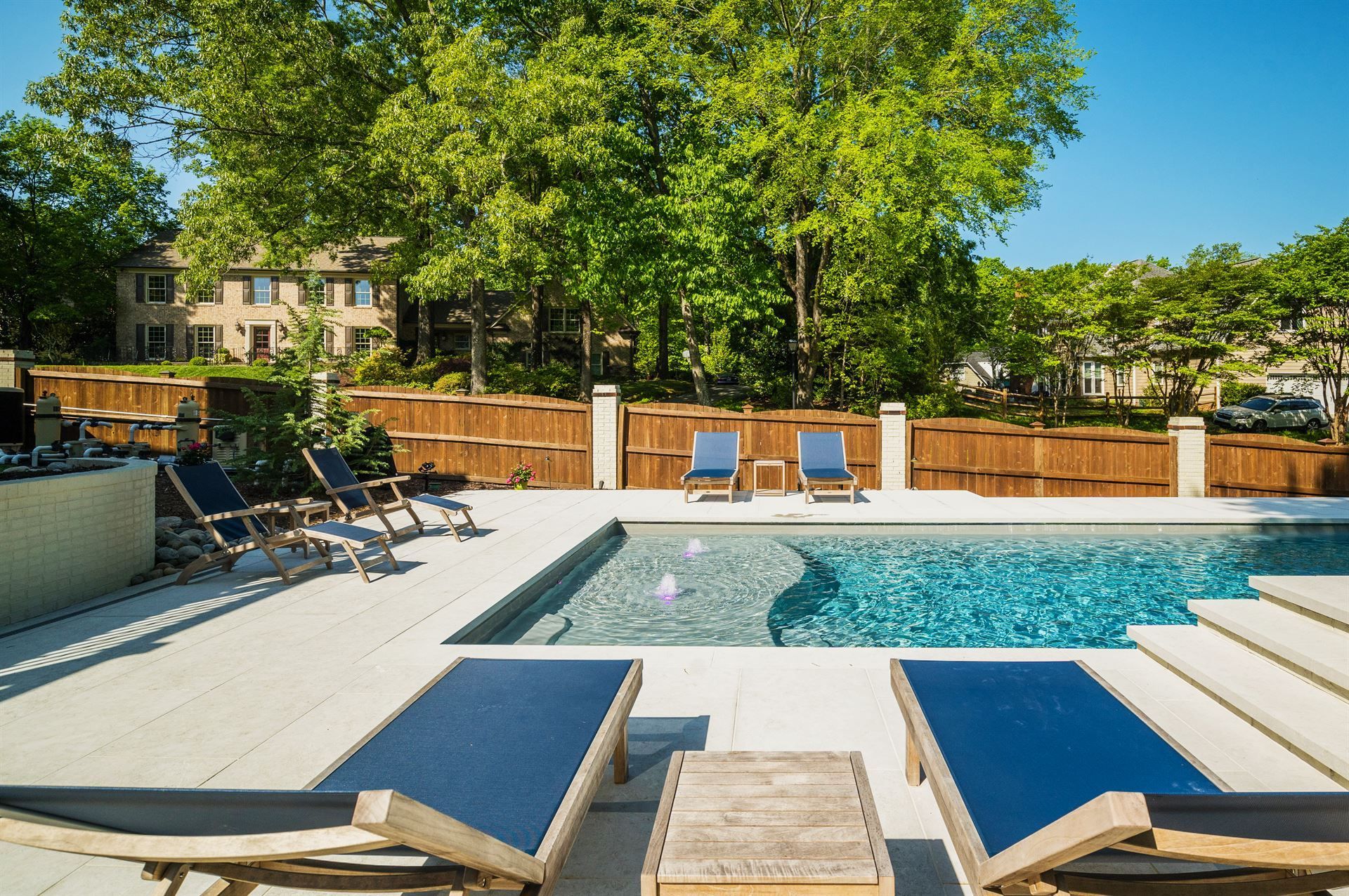 Backyard pool with lounge chairs, wooden fence, and trees in bright sunlight