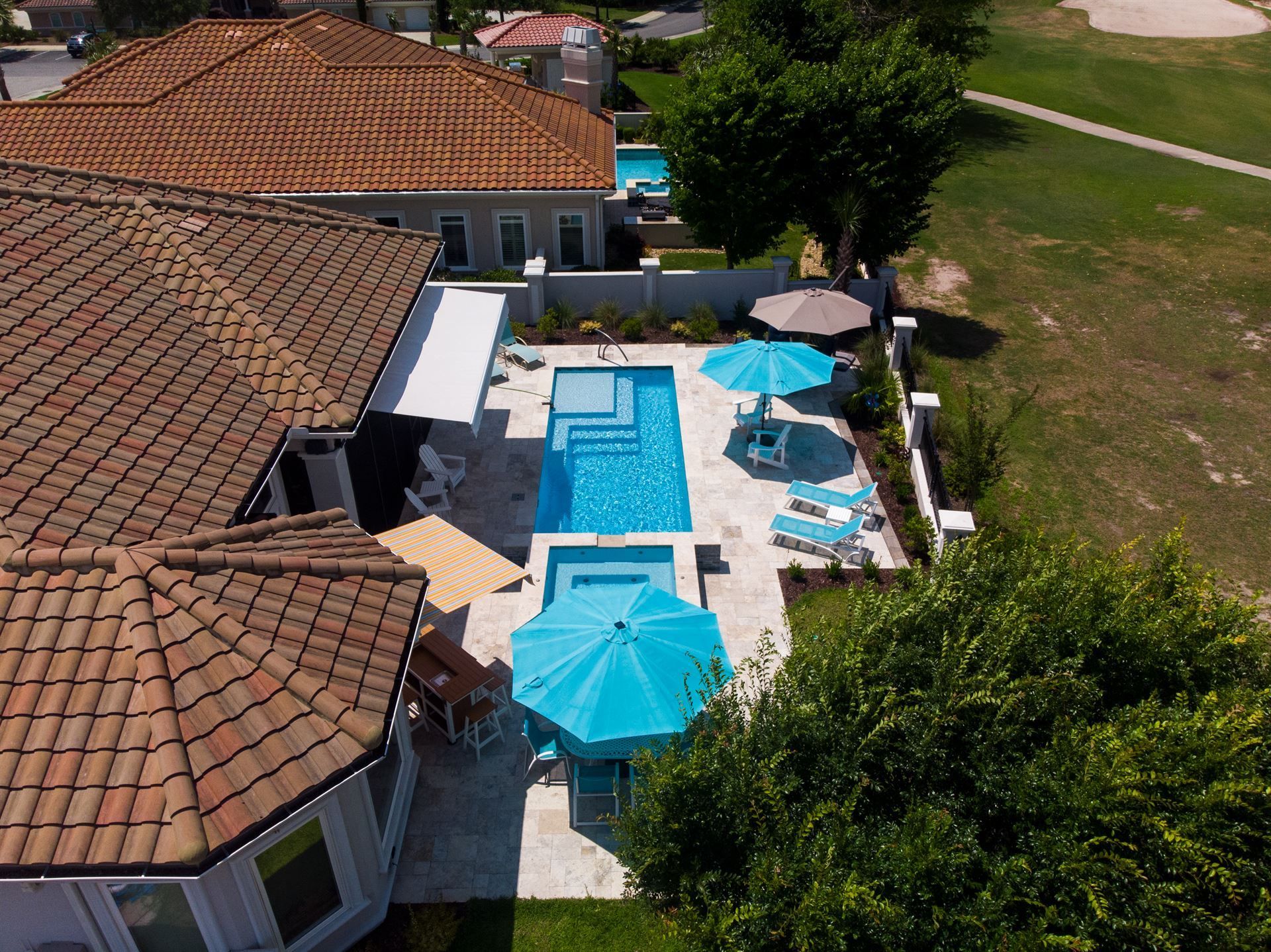 Aerial view of a house patio with a rectangular pool, turquoise umbrellas, and lounge chairs beside a yard.