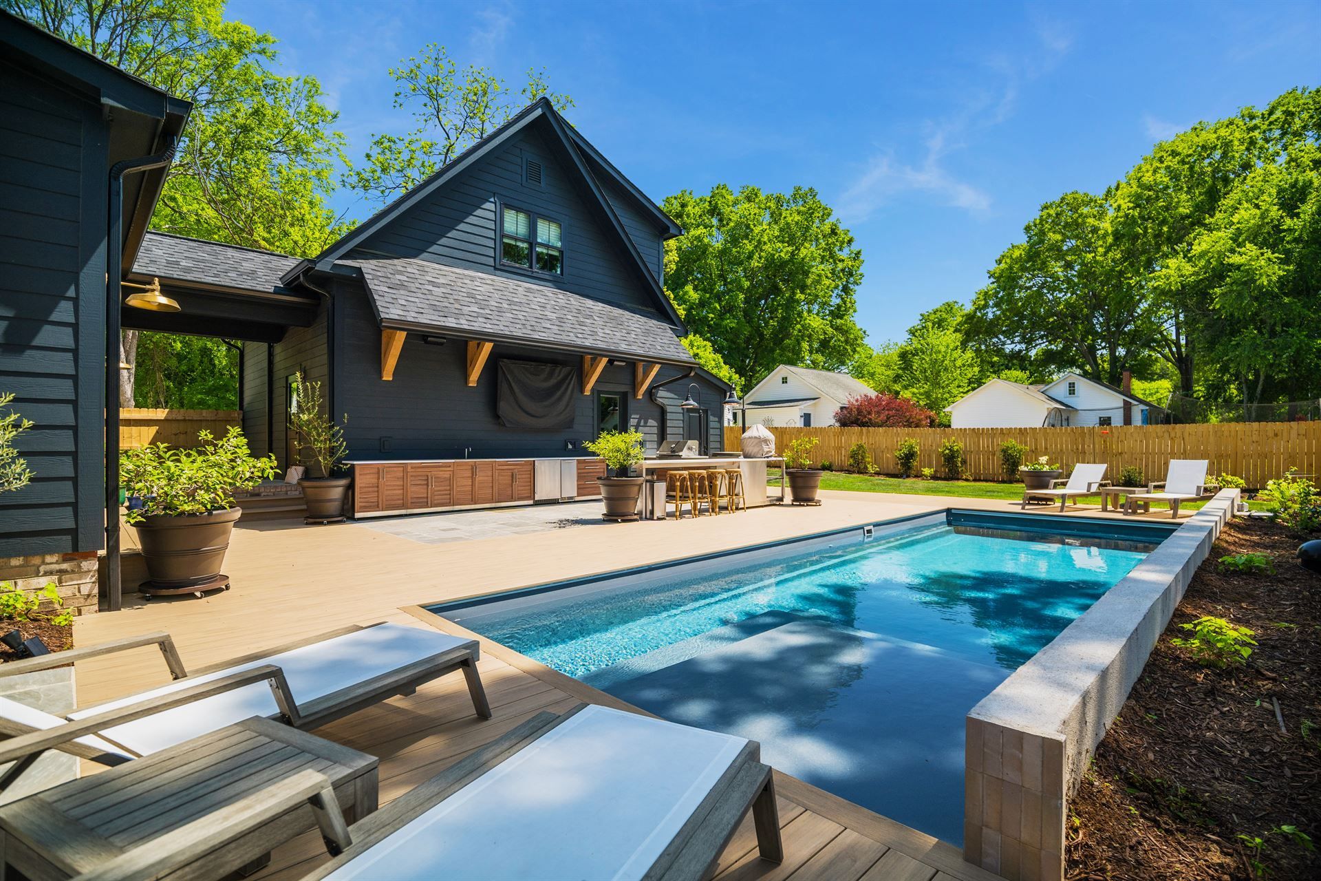 Modern backyard with a blue swimming pool, lounge chairs, and a dark house under sunny skies
