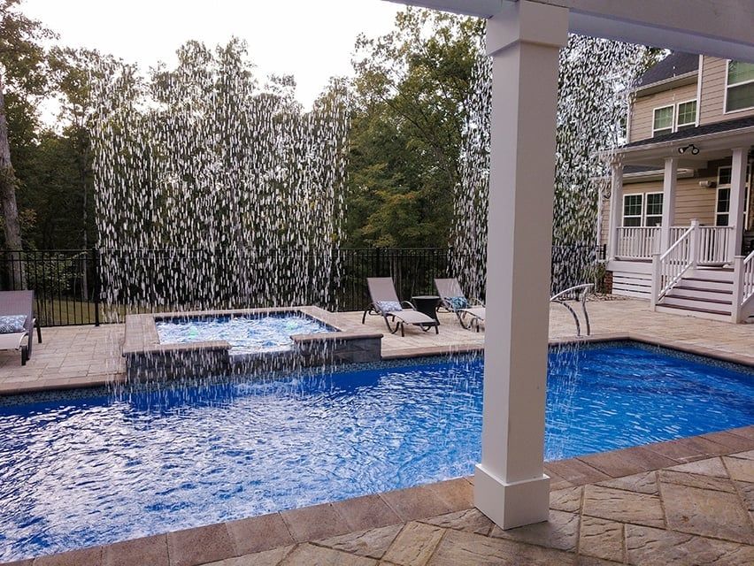 Backyard pool and hot tub beside a house, with lounge chairs and a stone patio