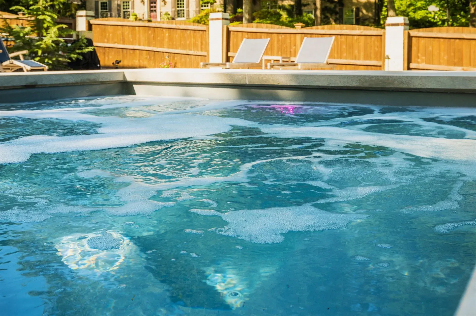 Outdoor hot tub with bubbling blue water and lounge chairs on a sunny deck