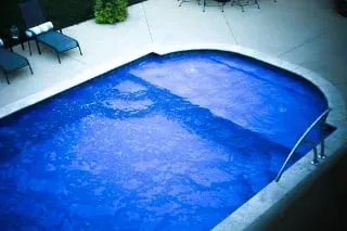 Blue swimming pool covered by a fitted safety cover, with lounge chairs nearby