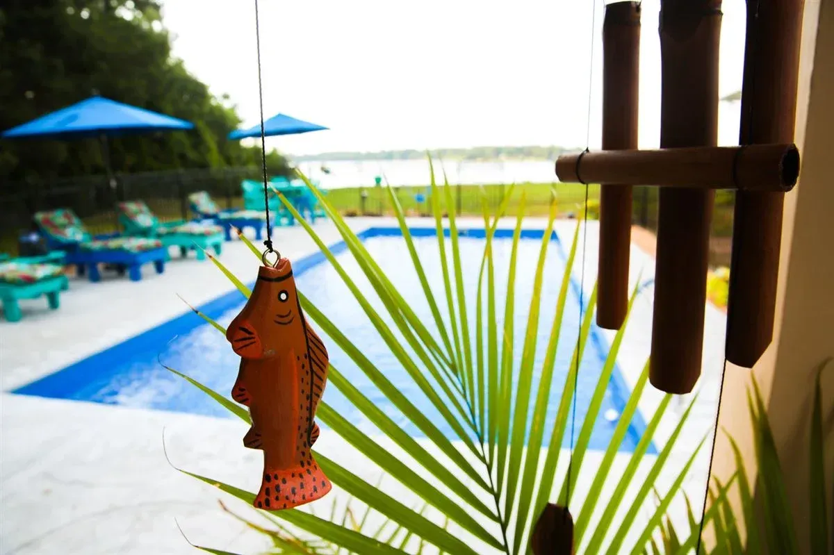 Orange fish ornament hanging near a pool with blue umbrellas and lounge chairs, palm fronds in the foreground