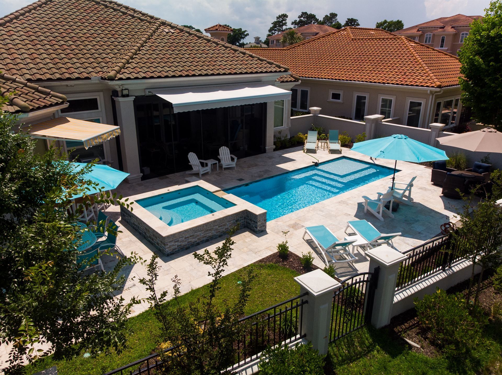 Modern backyard with a swimming pool, hot tub, patio seating, and blue umbrellas beside a tiled house