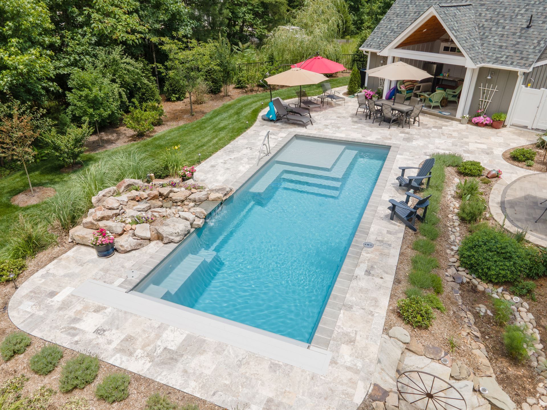 Backyard pool with stone patio, lounge chairs, and a covered outdoor seating area surrounded by greenery