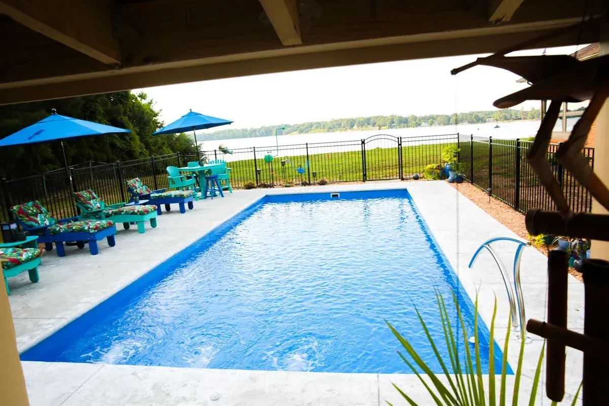 Covered outdoor swimming pool with blue water, lounge chairs, umbrellas, and a patio overlooking greenery