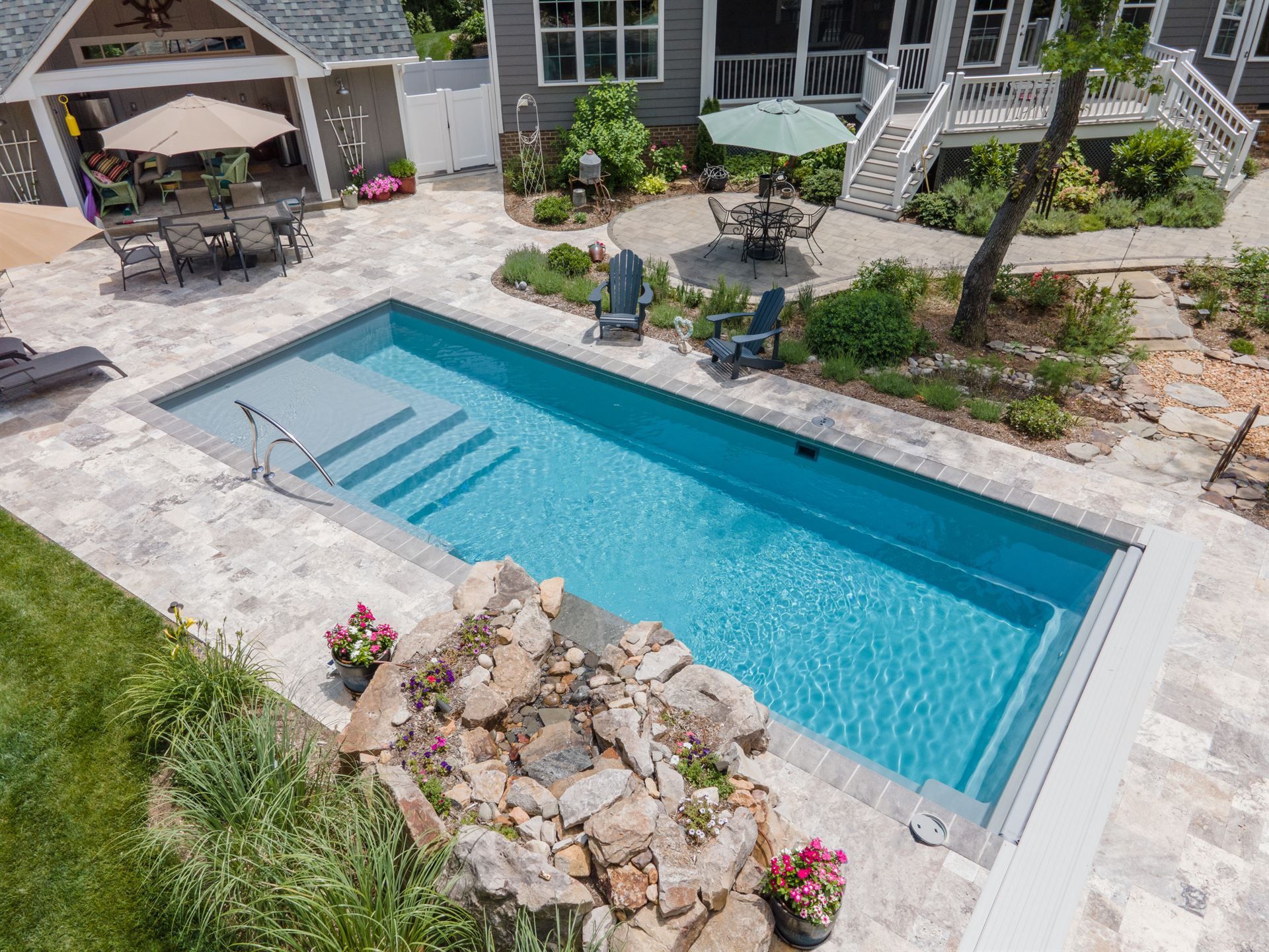 Backyard pool with blue water, stone patio, and landscaped garden beside a house