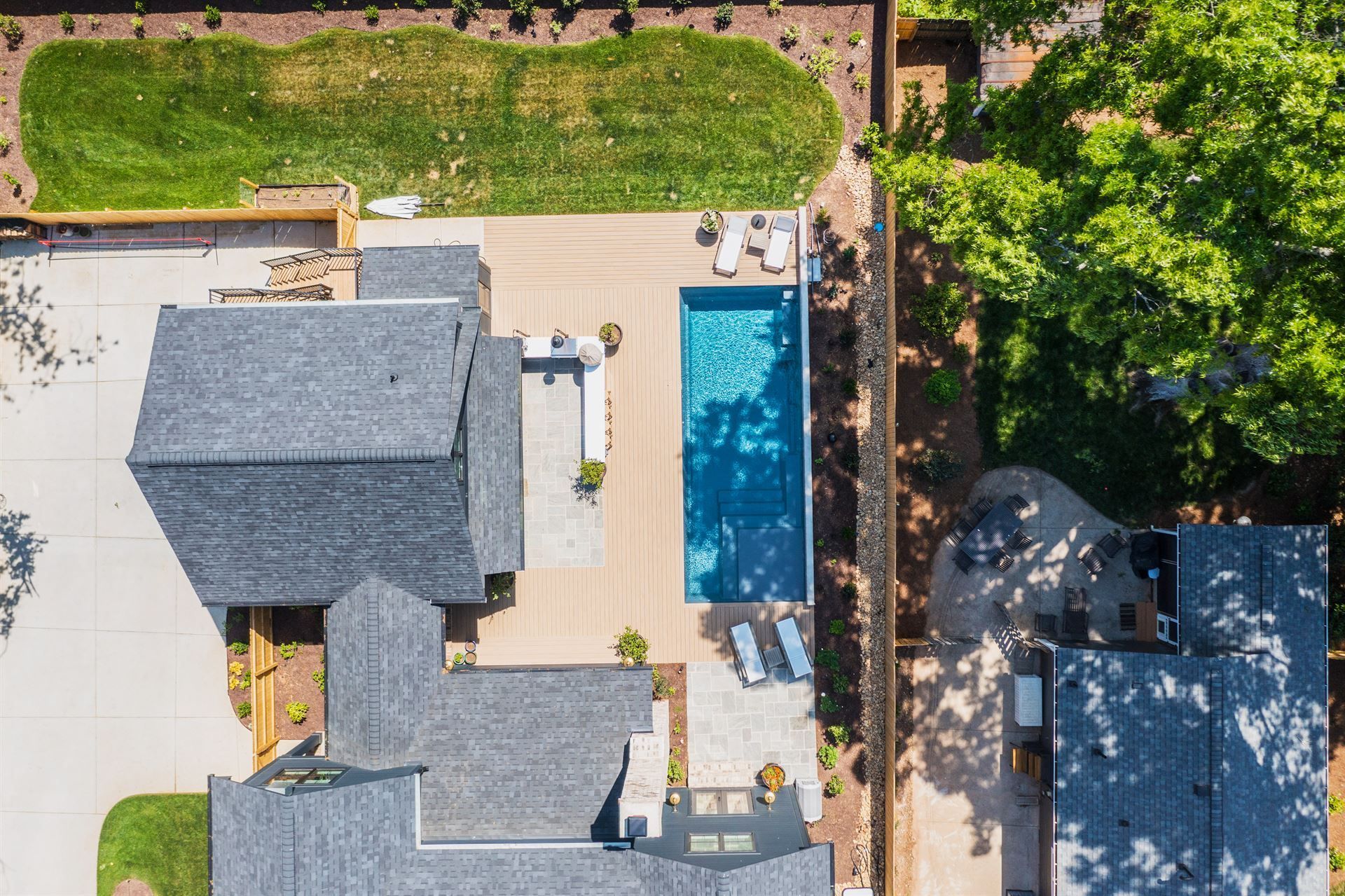 Aerial view of a backyard with a house, pool, patio, and surrounding trees.