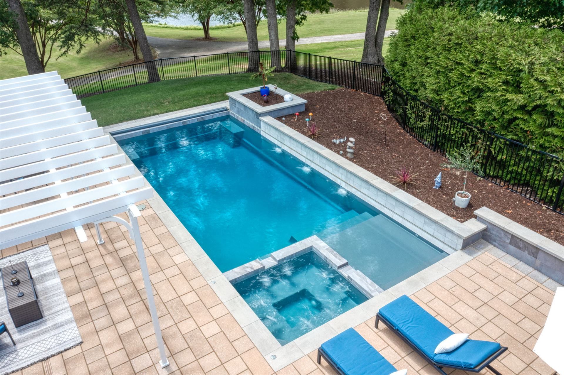 Backyard pool with a hot tub, lounge chairs, and a covered patio beside a hedge and lawn