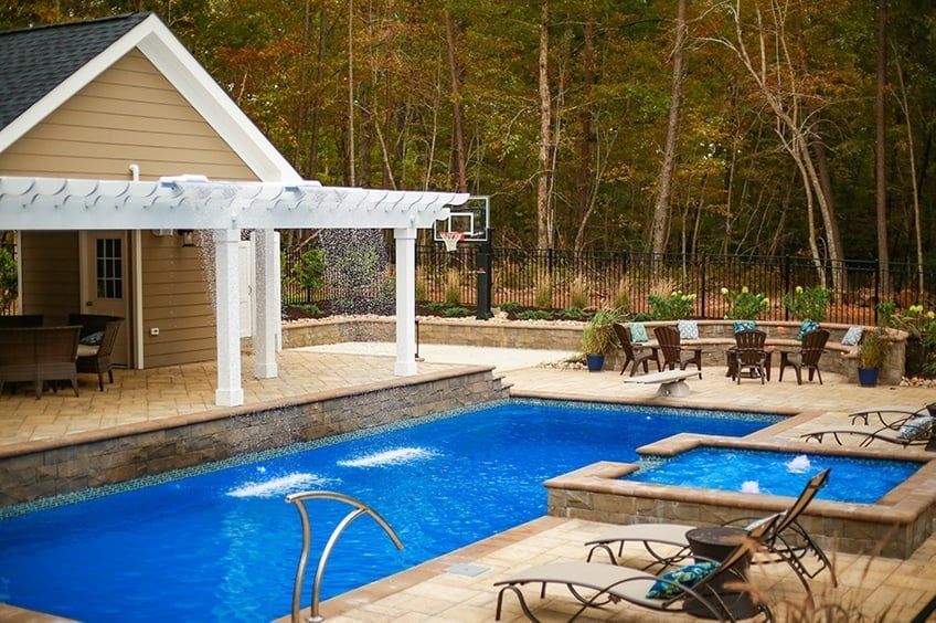 Backyard pool with blue water, lounge chairs, pergola, and patio beside a house and wooded yard