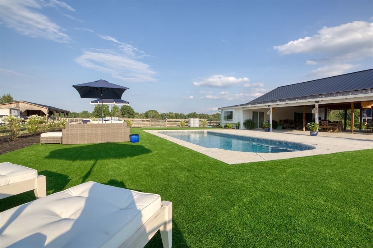 Modern backyard with green lawn, white patio furniture, pool, and open-air pavilion under a blue sky