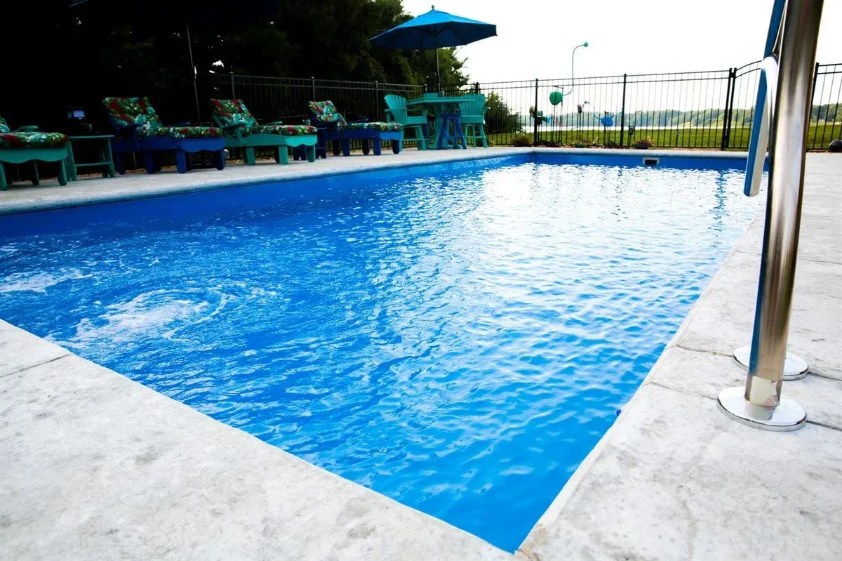 Blue outdoor swimming pool with lounge chairs and umbrellas beside the deck