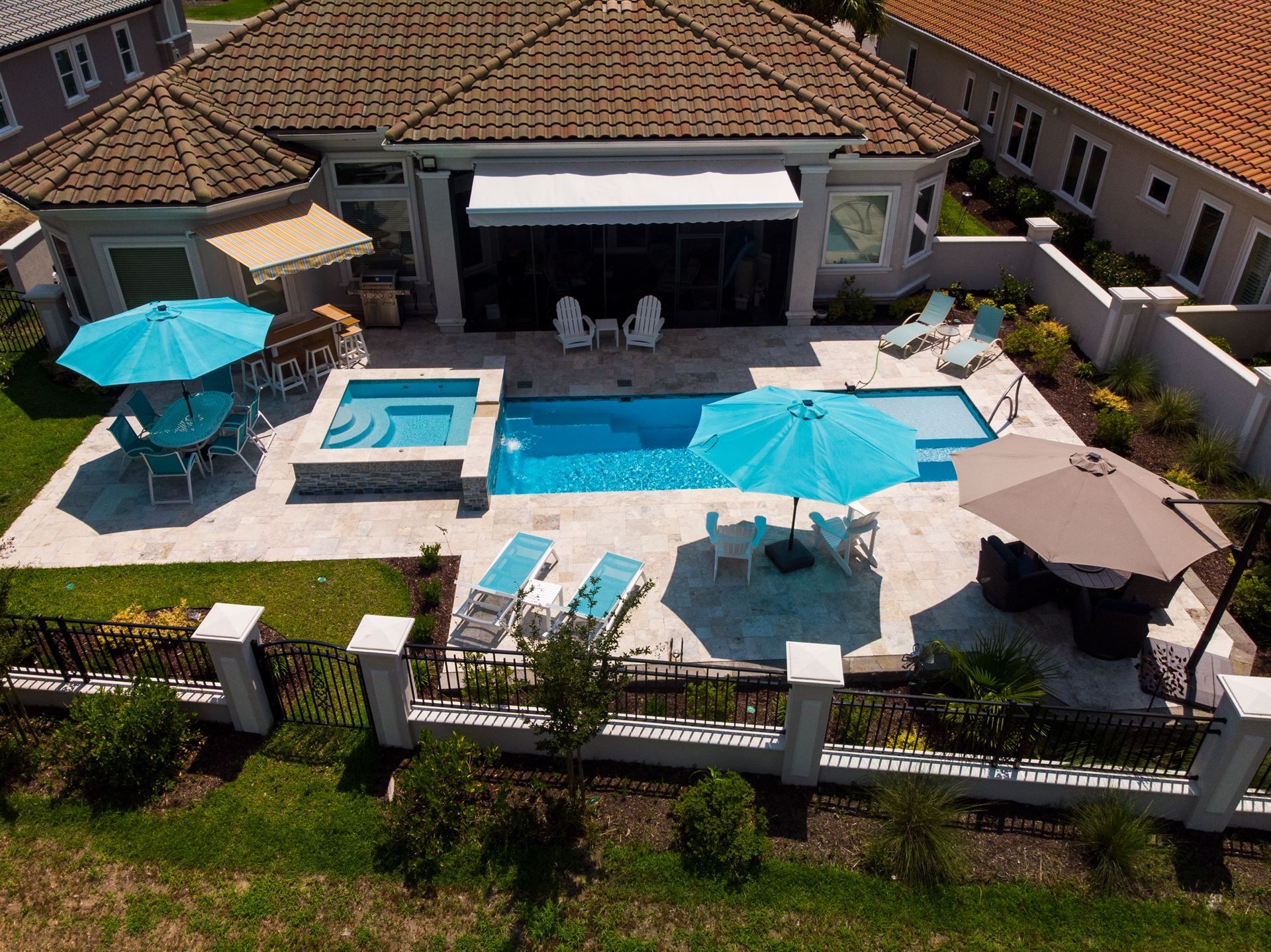 Aerial view of a luxury backyard with a pool, patio seating, umbrellas, and a covered outdoor lounge area