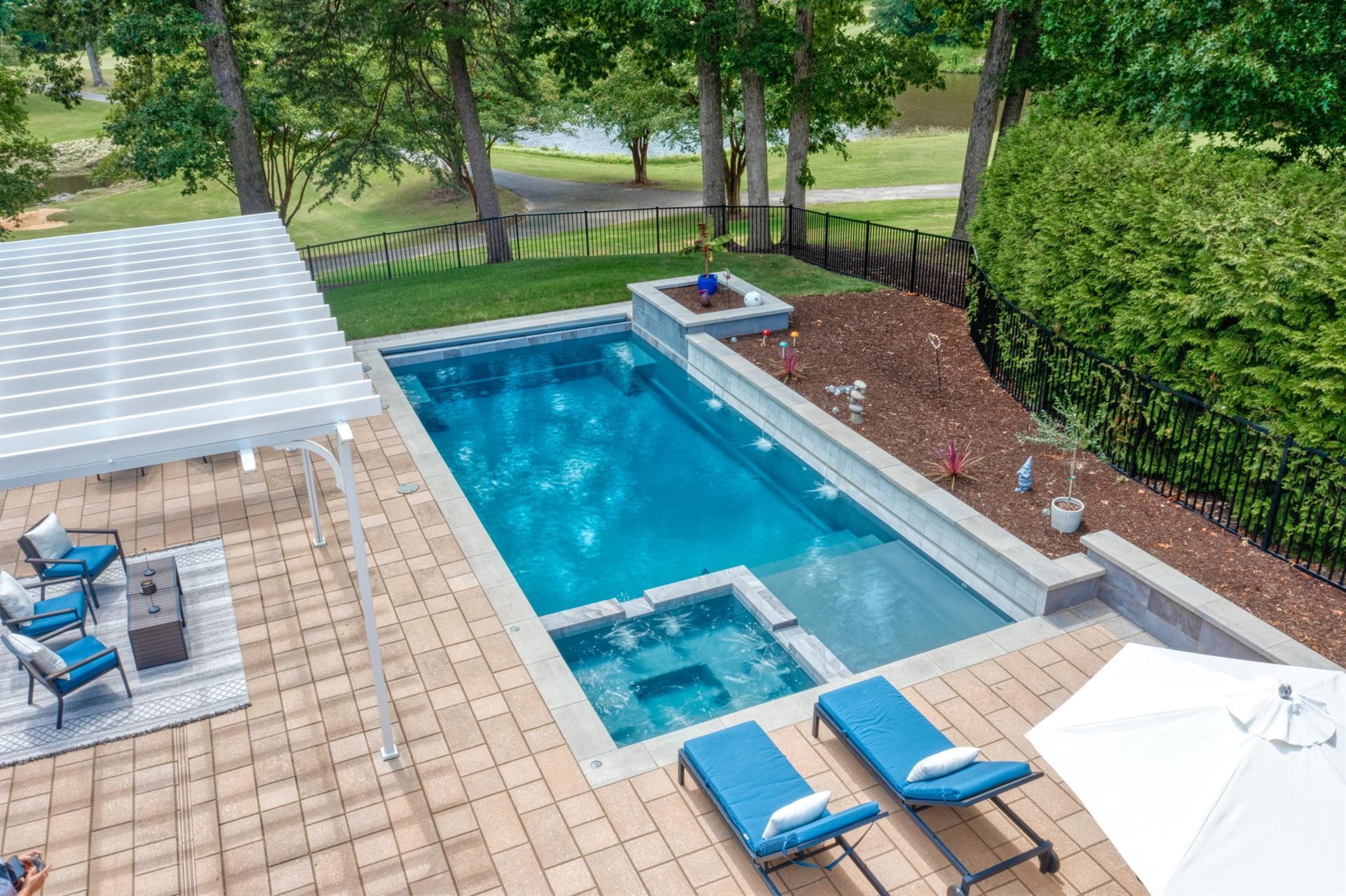 Backyard pool with blue lounge chairs, patio seating, and trees beside a landscaped yard